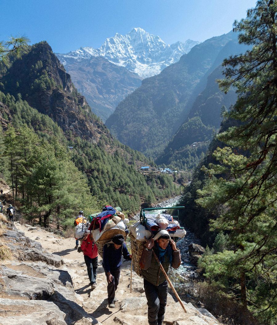 Porters carrying loaded baskets up a stone trail through the valley