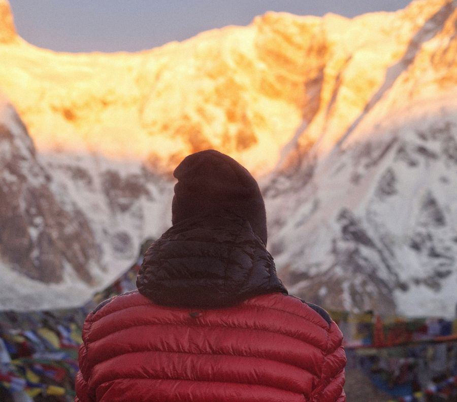 A figure in a red down jacket watching first light strike the summit