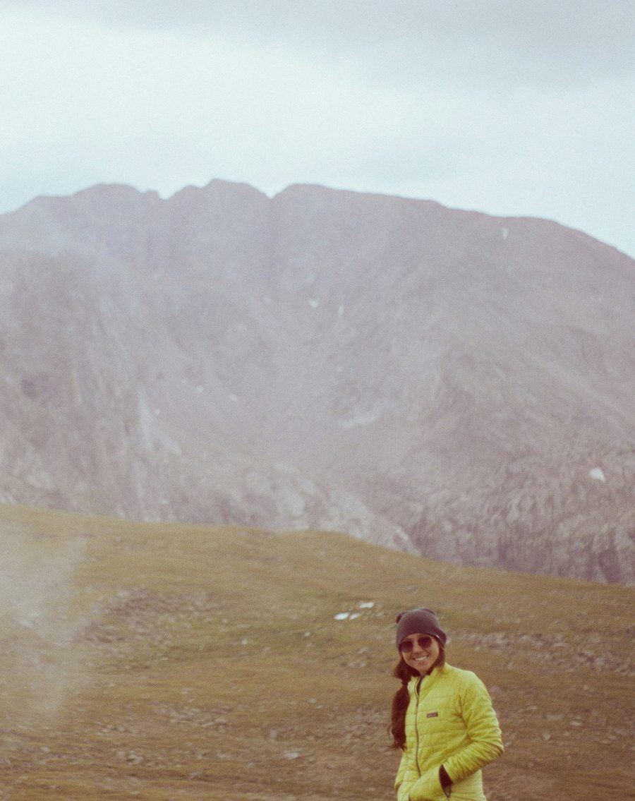 A trekker in a yellow jacket on a misty hillside below a ridge