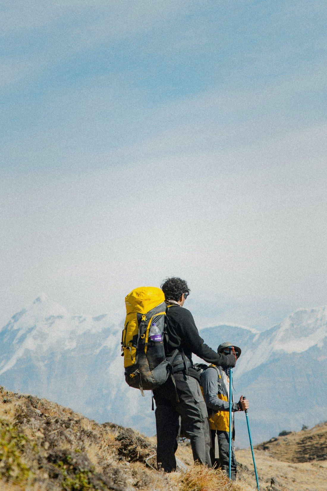 Two trekkers pausing on a ridge, snow peaks stretching behind them