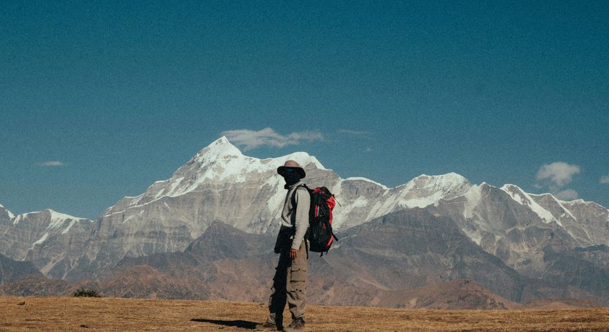 A trekker standing alone on open ground before a wall of snow peaks